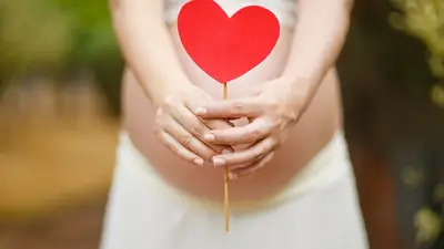 A pregnant woman holding a paper heart in front of her belly